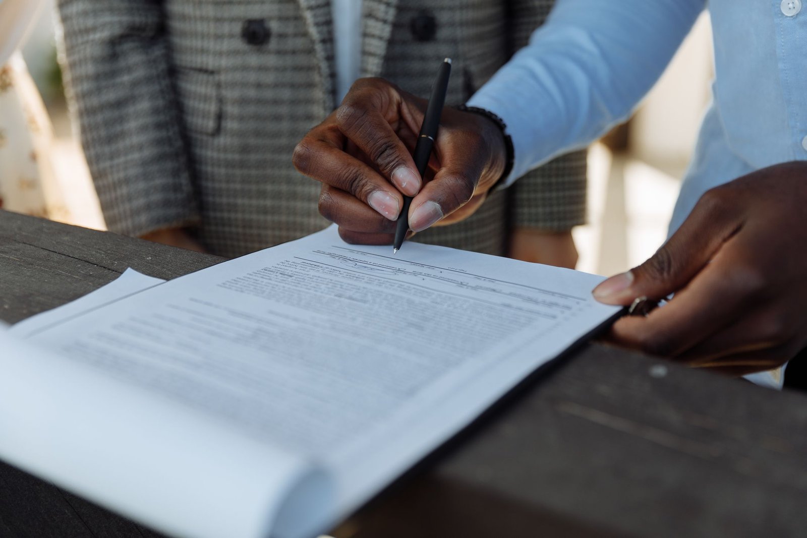 A hand signing a white page on a dark timber desk