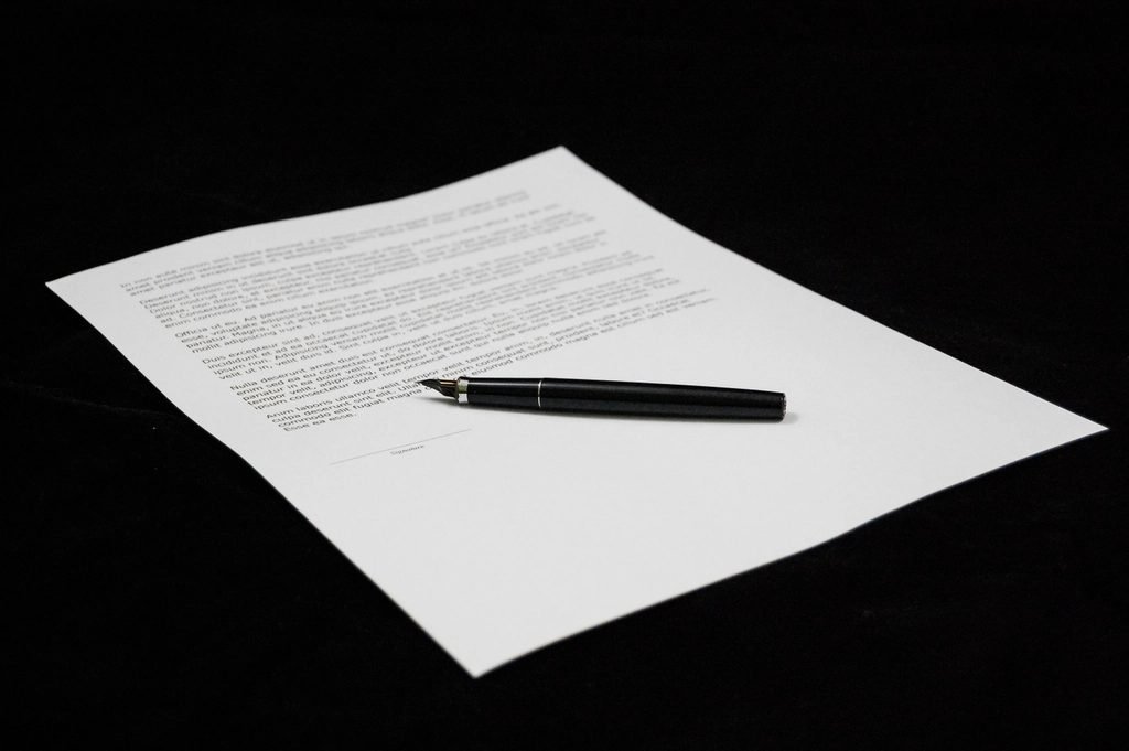 A single printed page on a dark surface, a fountain pen lying above the signature line