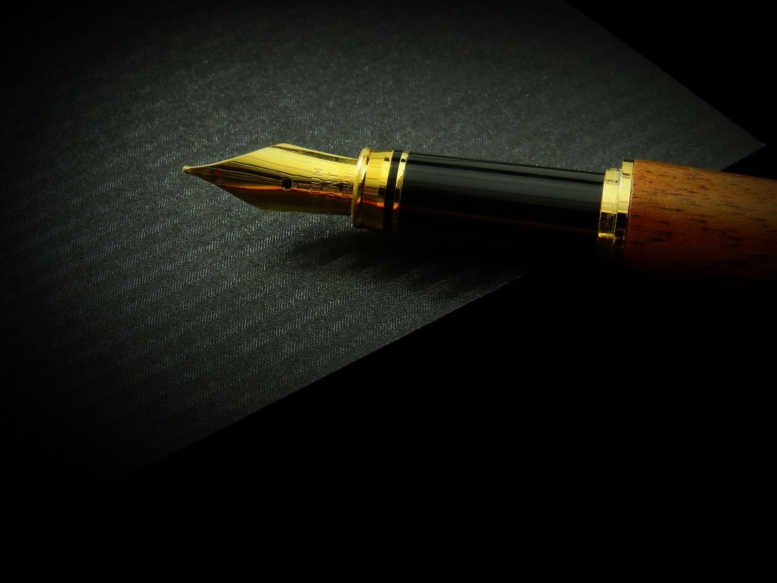 A gold fountain pen nib resting on dark textured paper