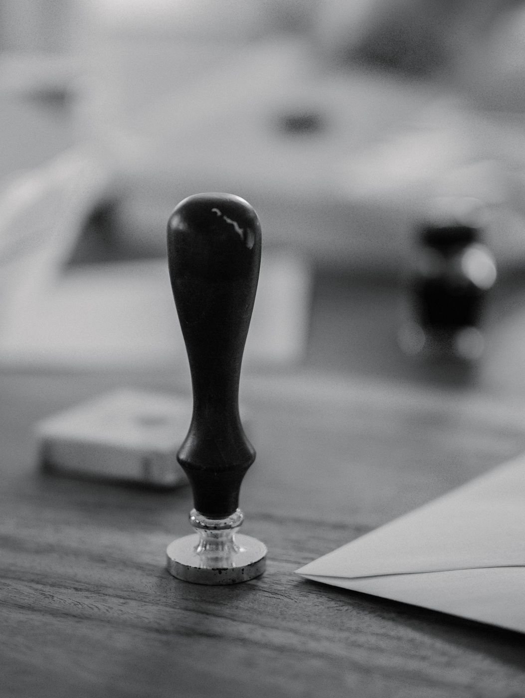 A wooden seal stamp standing on a desk beside an envelope, in black and white