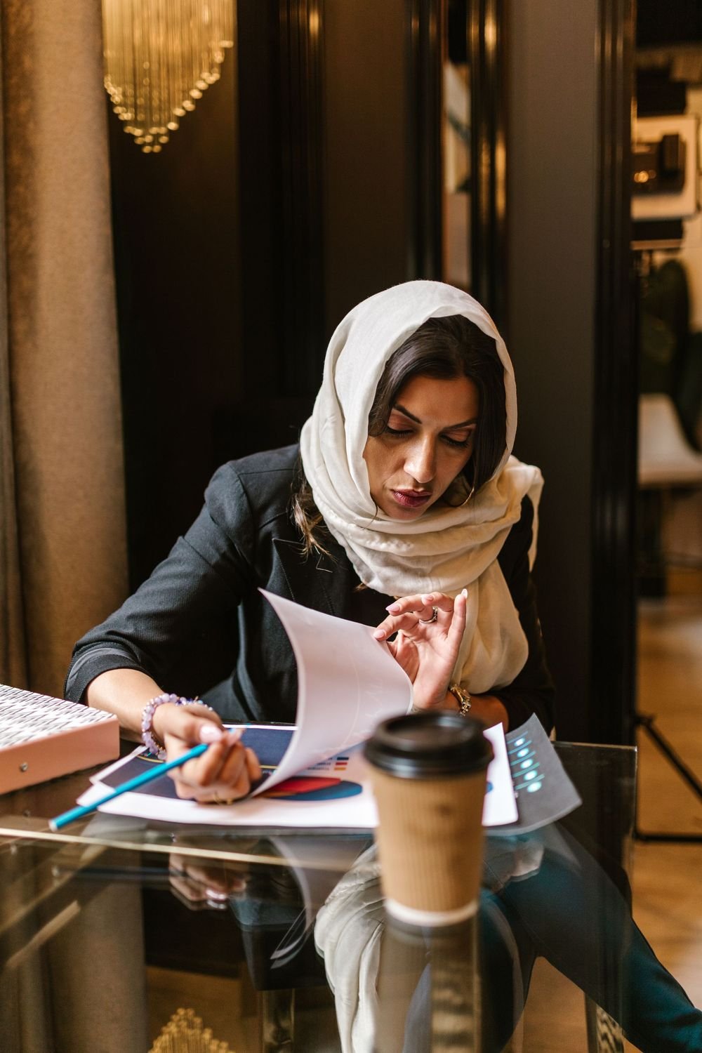 A woman in a white headscarf reading through documents at a desk